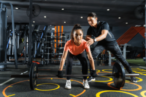 A man and a woman lifting a barbell in a gym.